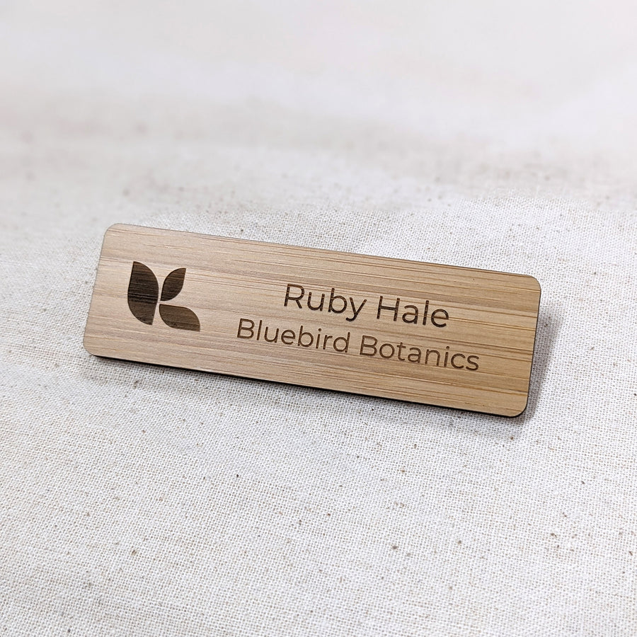 Wooden name badge with engraved text and logo on a light fabric background