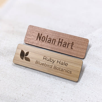 Two wooden name badges with engraved text on a light fabric background