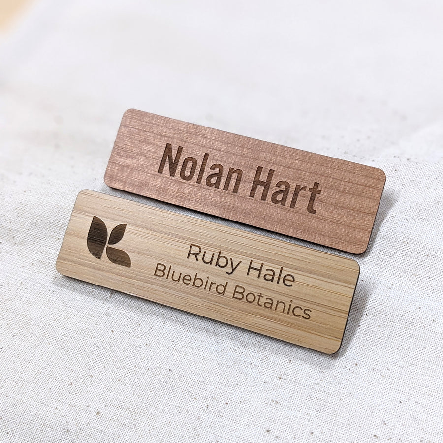 Two wooden name badges with engraved text on a light fabric background