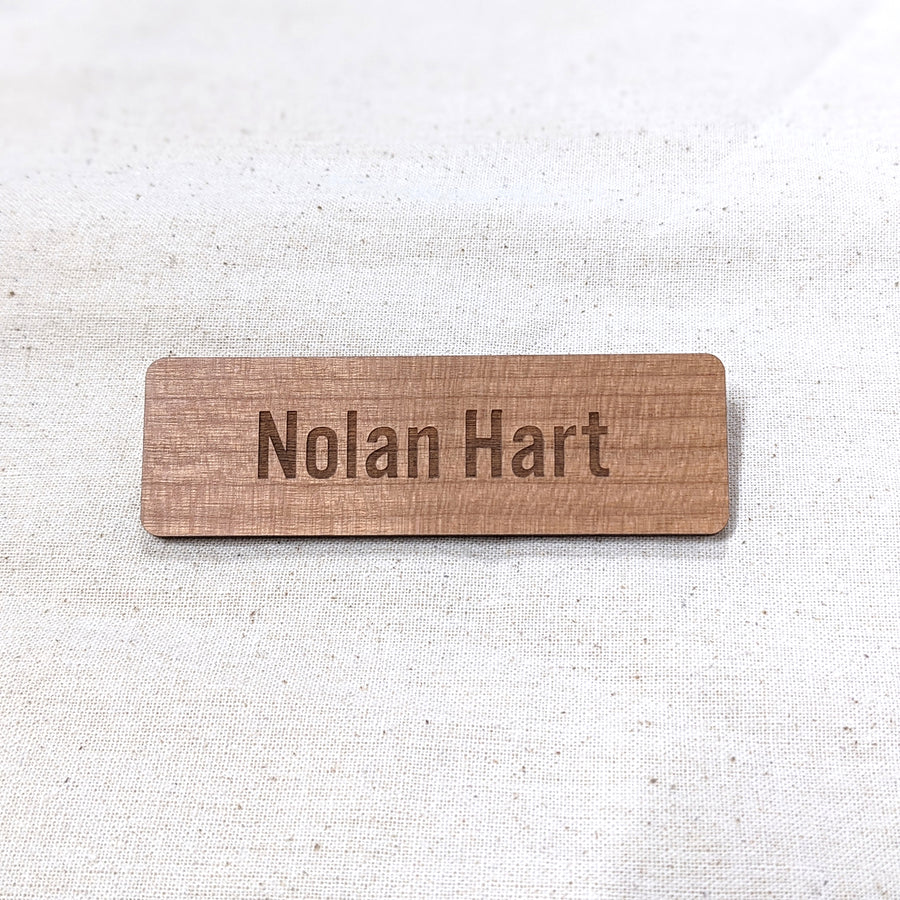 Wooden name badge with engraved text 'Nolan Hart' on a light fabric background