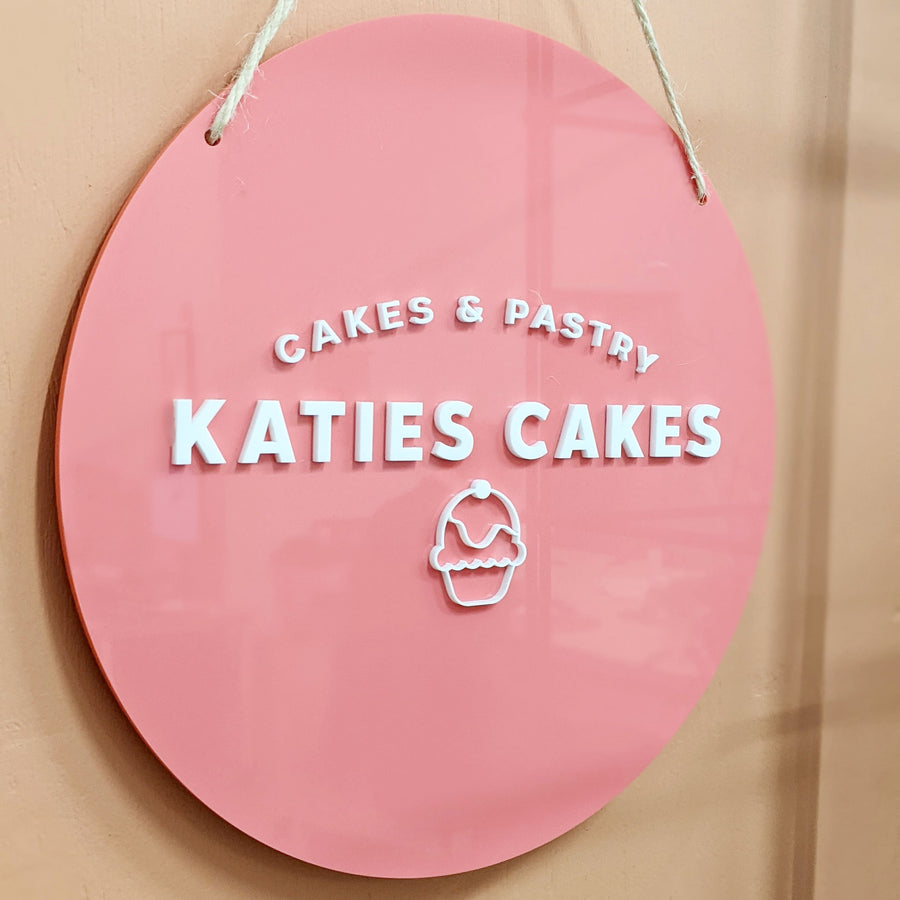 cupcake logo on pink acrylic hanging from cord